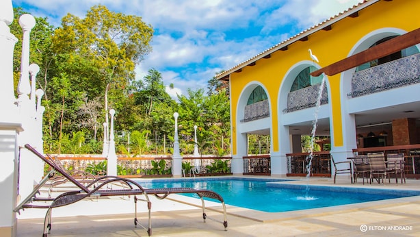 A pool area with lounge chairs, a yellow building with arched windows, and a clear blue sky. - Terra dos Diamantes (Lençóis)