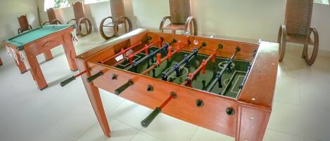 A foosball table in a room with tiled flooring and wooden chairs.