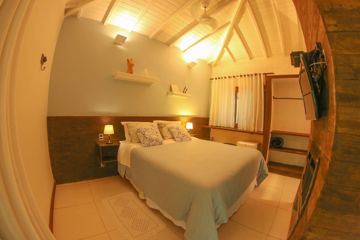 A bedroom with a bed, bedside tables, a nightstand, a shelf with decorative items, and a wooden wall.