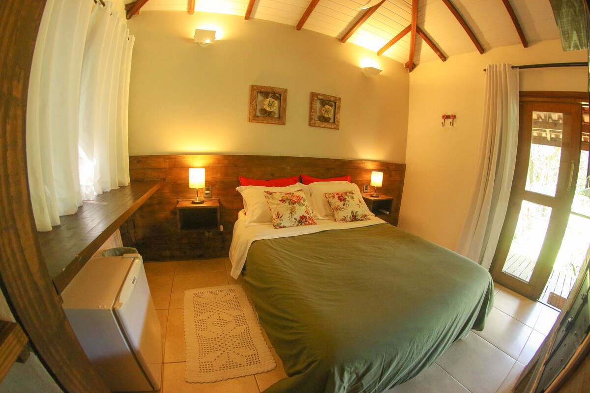 A bedroom with a bed, two nightstands, a refrigerator, and a door leading outside.