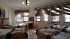 Una habitación de hotel con cuatro camas individuales, una televisión y ventanas amplias con persianas.