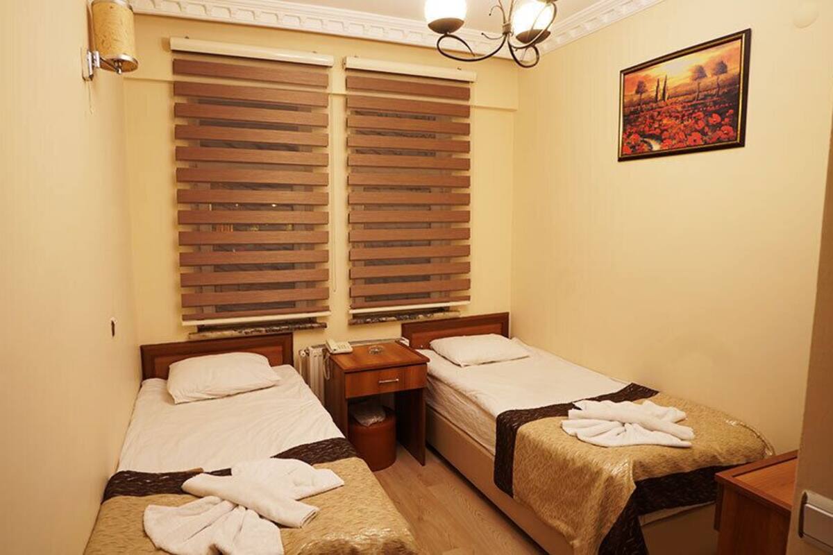 A small, cozy room with two single beds, a nightstand, a lamp, and a painting on the wall.