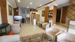 Un vestíbulo de hotel con televisión, zona de estar y una escalera que sube a otro piso.