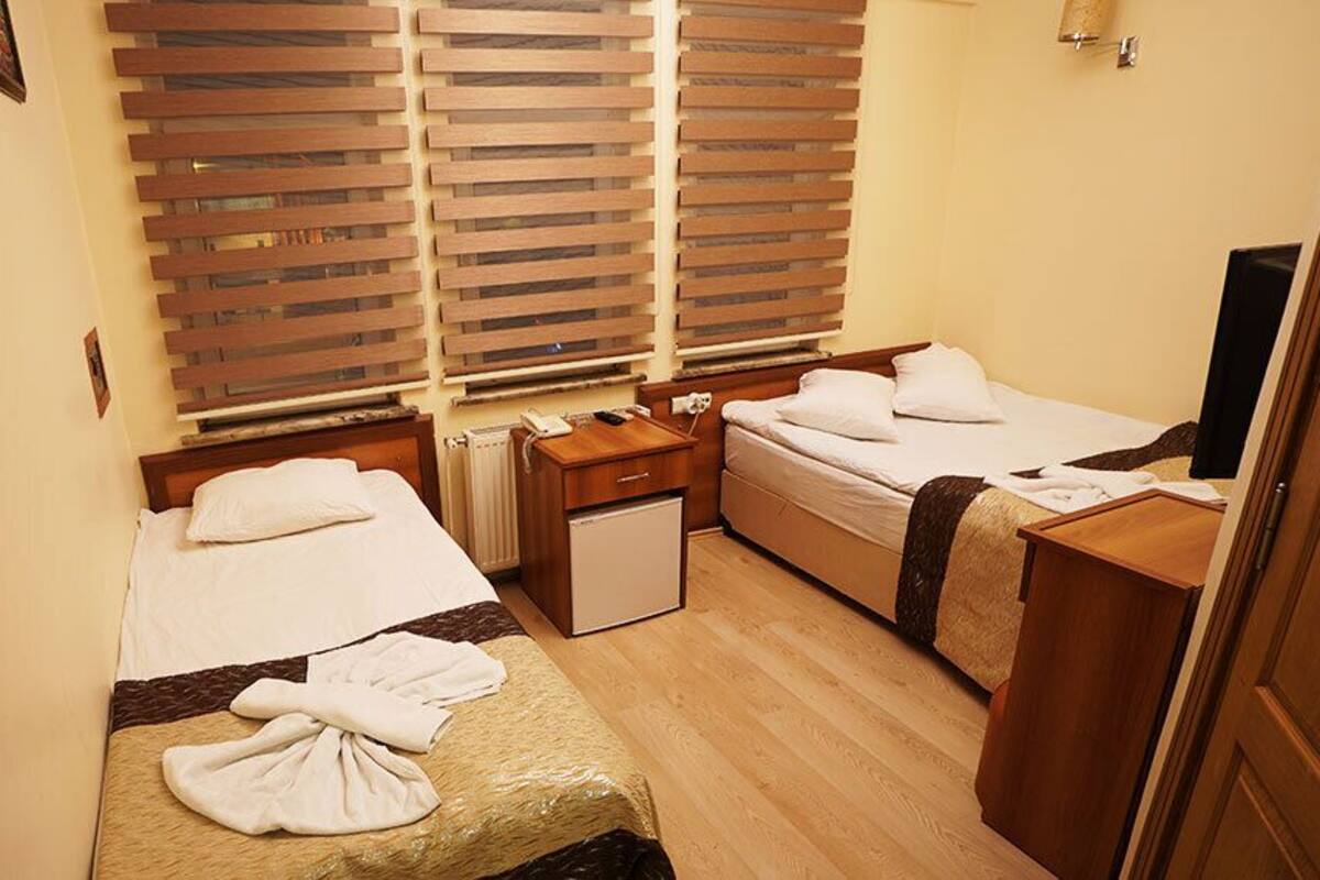 A hotel room with two beds, a small desk, a TV, and a window with blinds.