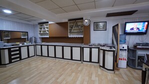 Una cocina con piso de madera, armarios blancos y un televisor montado en la pared.