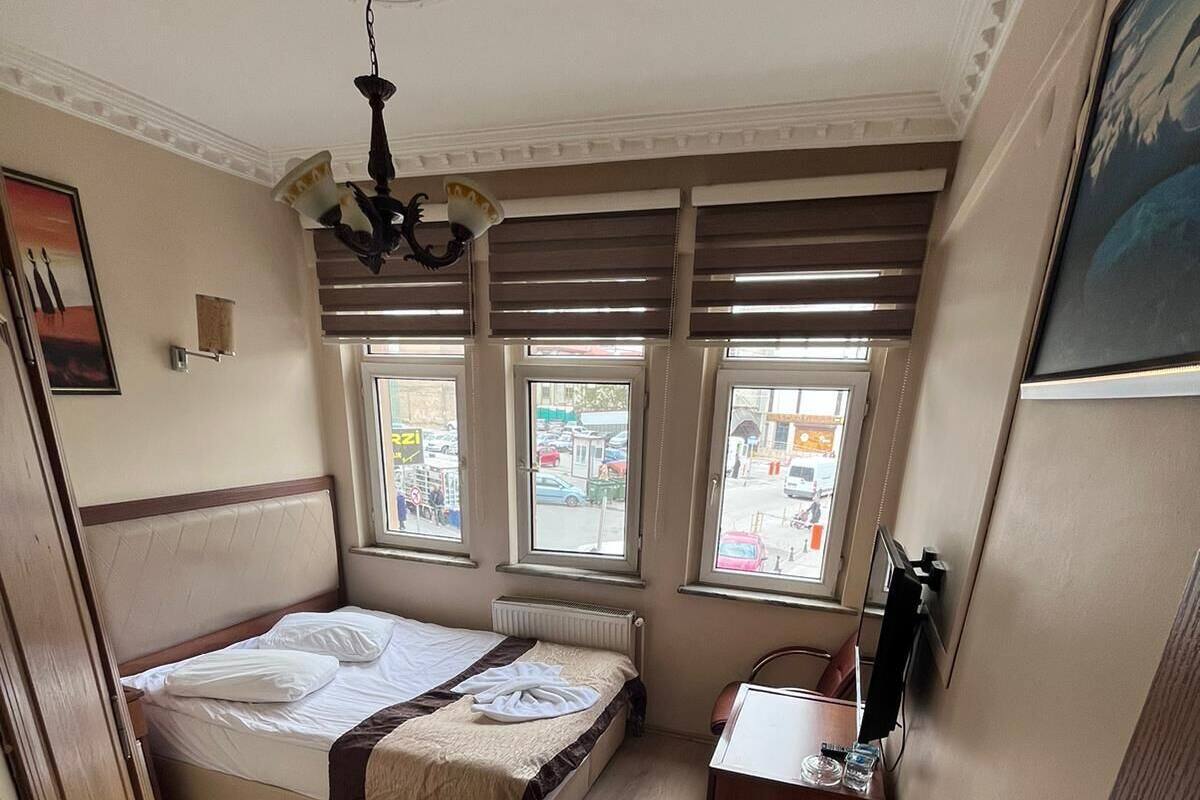 A bedroom with a bed, a desk, and a radiator. There are three windows and a ceiling fan.