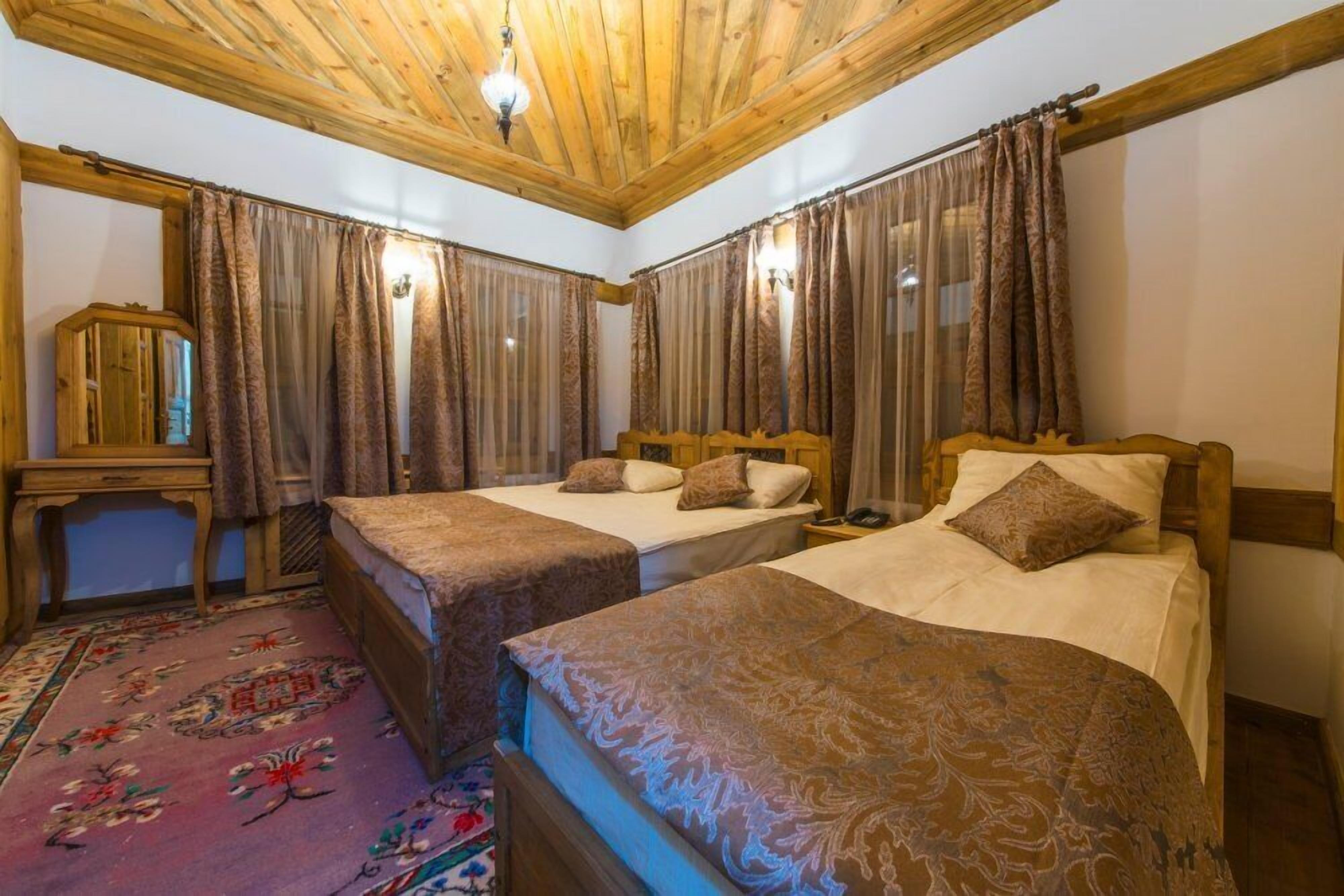 A room with three beds, wooden ceiling, and a floral carpet.