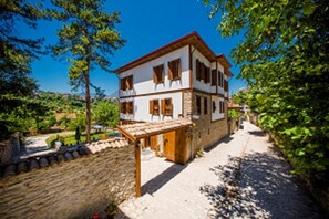 A two-story building with a stone facade and wooden shutters, a paved driveway, and a stone wall. - Akbulut Konak (Safranbolu)