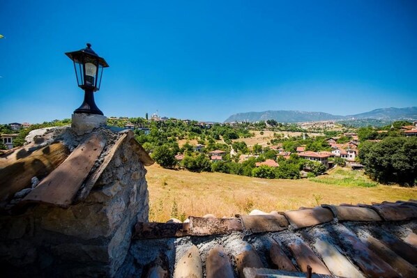 A stone wall with a metal lantern and a tiled roof overlooking a village with houses and greenery. - Akbulut Konak (Safranbolu)