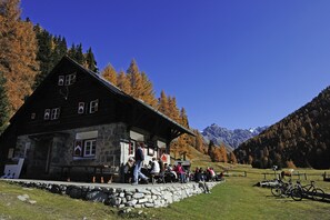 A stone building with a wooden roof, a sign reading "VARDUS CH", and a stone wall in front.