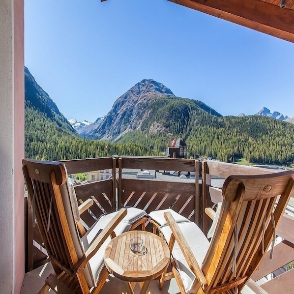 A wooden deck with a table and chairs, overlooking a mountainous landscape with a clear sky.