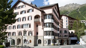 A pink and white hotel with multiple balconies and arched windows, surrounded by mountains. - Hotel Rosatsch Sleep Only (Pontresina)