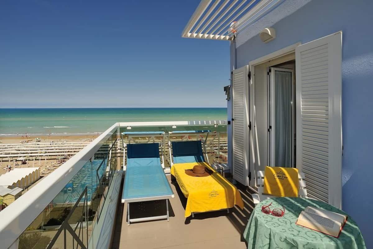 A balcony with two beds, a table with a hat and sunglasses, and a view of the beach and ocean.