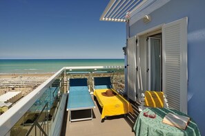 A balcony with two beds, a table with a hat and sunglasses, and a view of the beach and ocean. - Hotel Cigno D'Oro (Riccione)