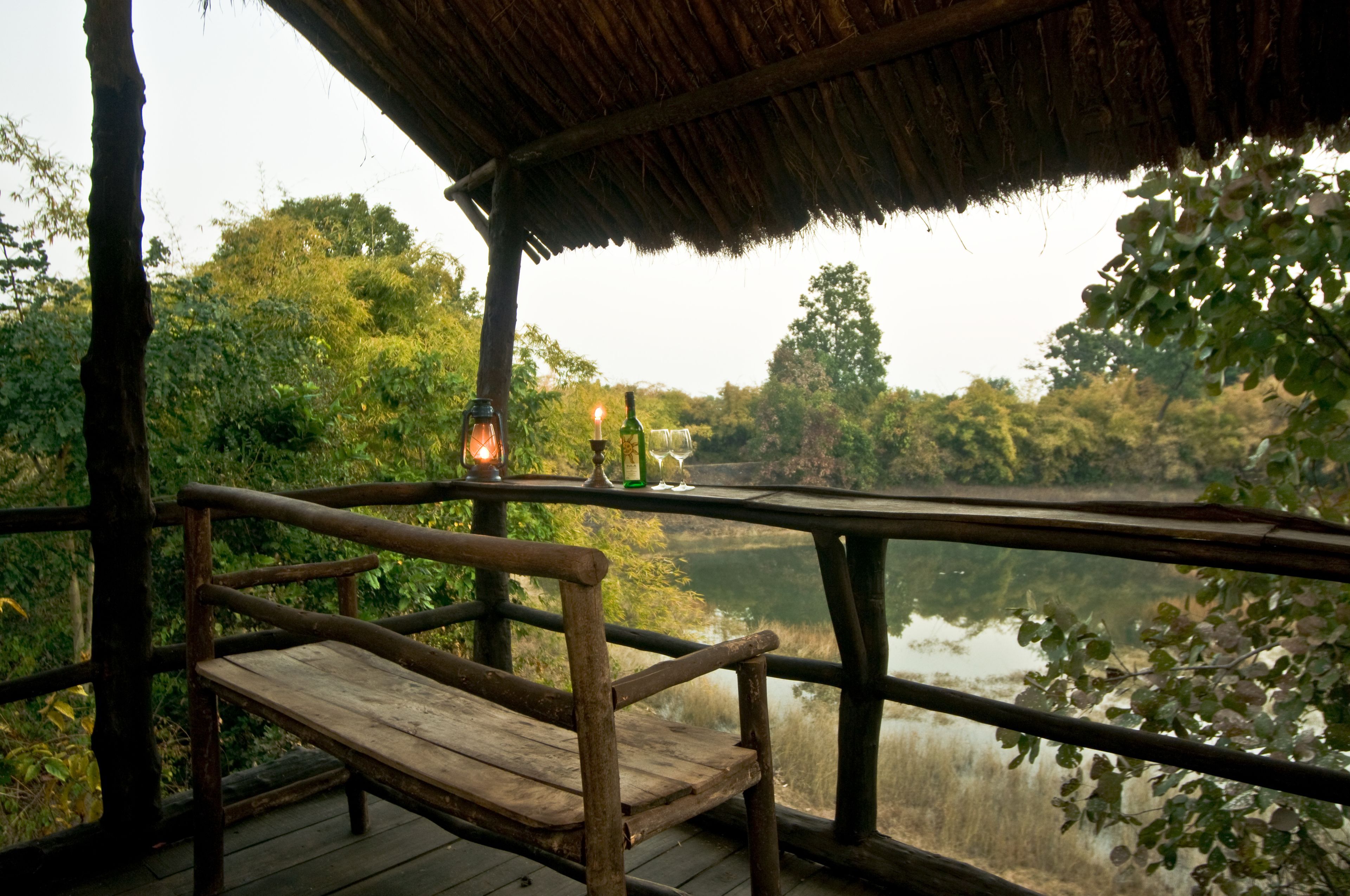 Un banco de madera bajo un tejado de paja con vistas a una masa de agua tranquila, rodeado de abundante vegetación.