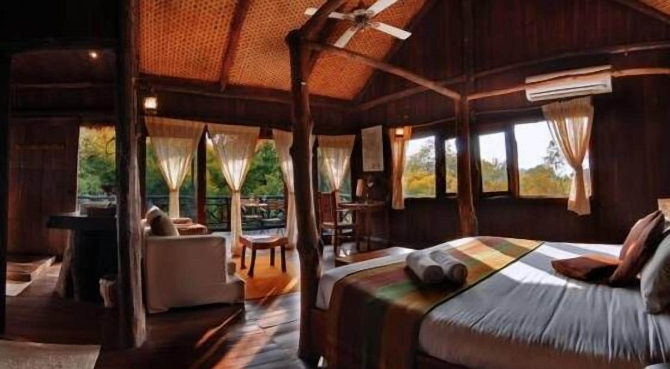Une chambre spacieuse avec un grand lit, un coin salon avec une table et une vue sur l’extérieur grâce à de grandes fenêtres.