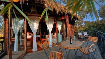 A wooden deck with outdoor seating and a thatched-roof structure with curtains.