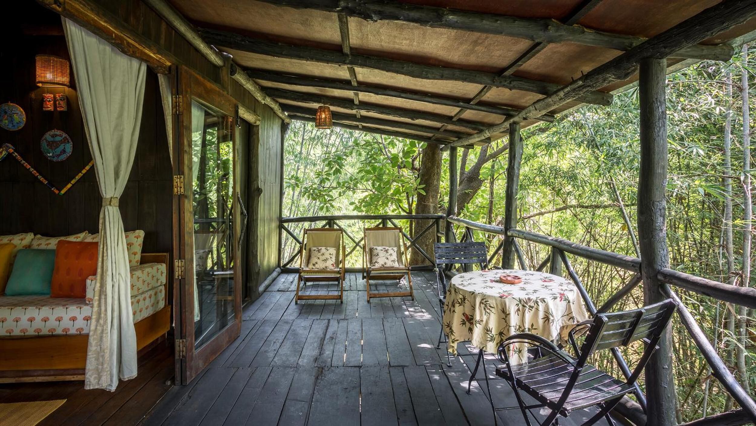 Una terraza de madera con un área de estar techada, que incluye un sofá y dos sillas, además de una mesa pequeña con mantel floral.