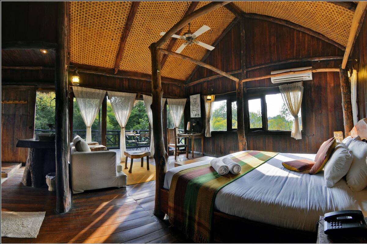 A rustic wooden cabin with a large bed, a dining area, and a view of the outdoors.