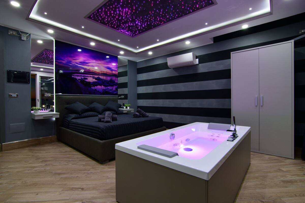 Un dormitorio moderno con una cama grande, un jacuzzi integrado, un techo estrellado y un mural con vistas a la ciudad.