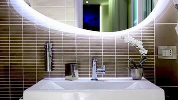 Un baño moderno con un lavamanos grande rectangular, un grifo cromado, un espejo con luz e una orquídea en maceta.