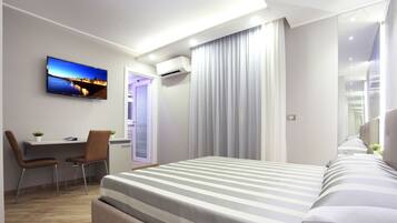 Una habitación de hotel moderna con una cama grande, un escritorio con sillas, un televisor en la pared y un equipo de aire acondicionado.