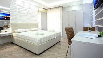 A modern hotel room with a large bed, a desk with a laptop, a chair, and a TV mounted on the wall.