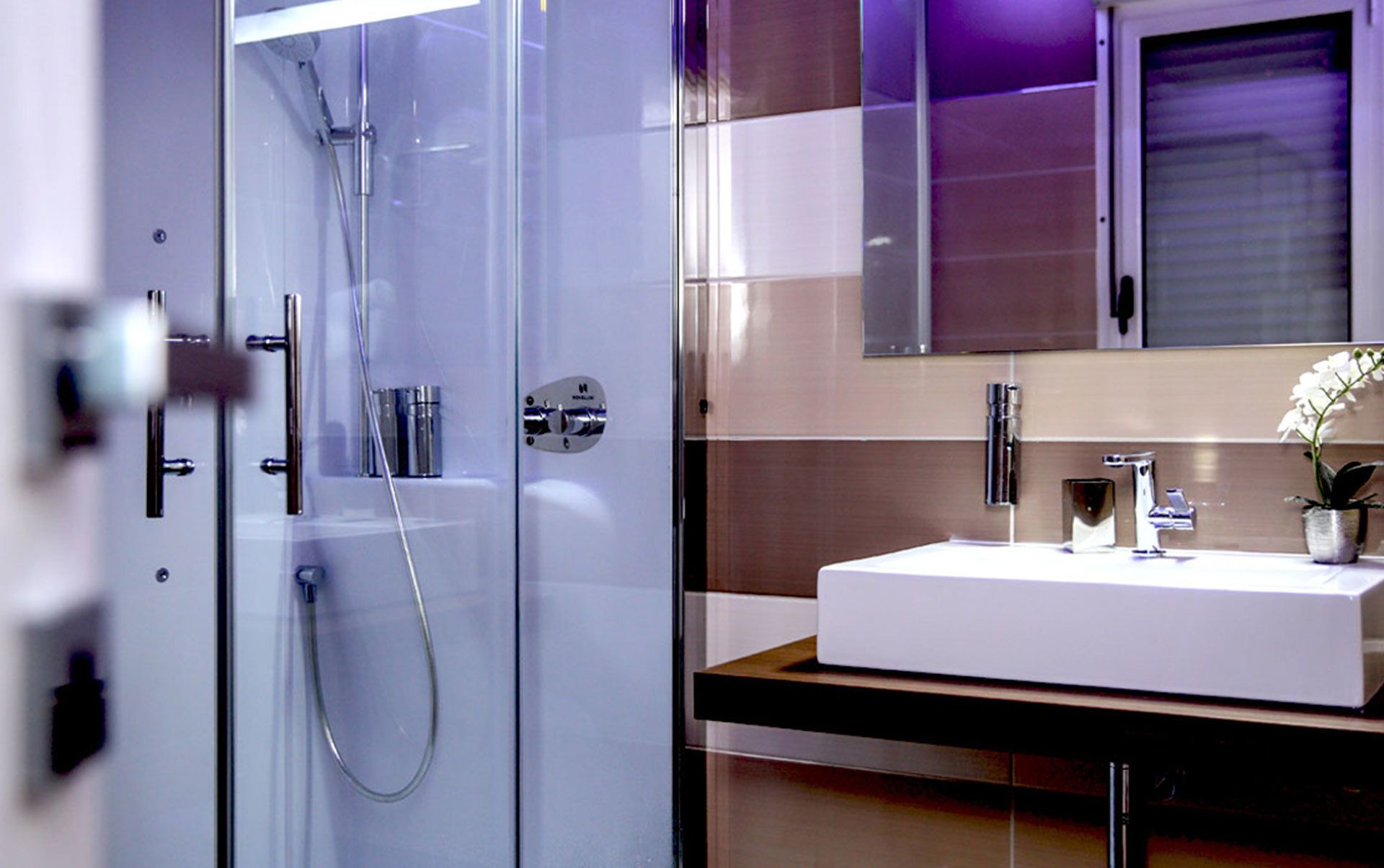 Un baño moderno con ducha de vidrio, un lavamanos blanco y un espejo encima.