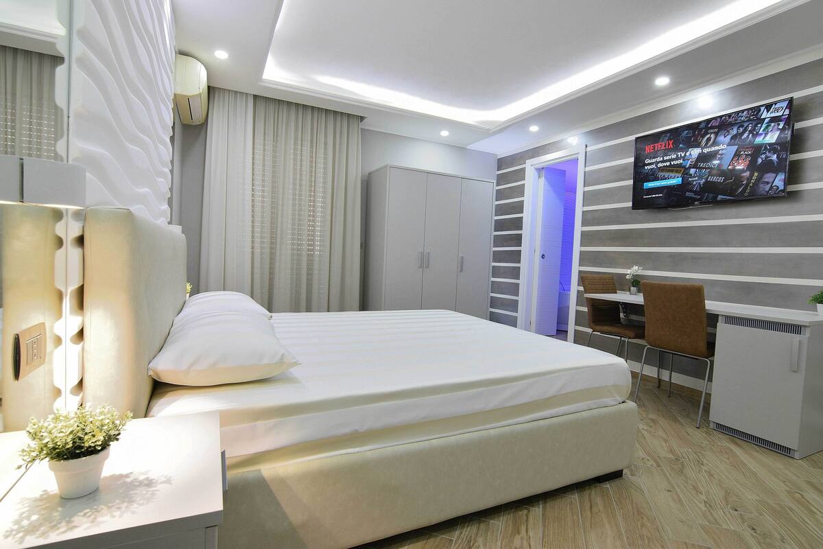 Un dormitorio moderno con cama, mesita de noche y televisión montada en la pared.