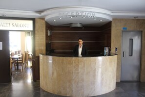 Un mostrador de recepción con un cartel que dice "RECEPTION" y un cartel de "ALTI SALONU" al fondo.