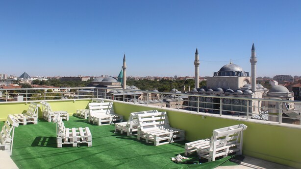 A rooftop terrace with white lounge chairs and a green artificial turf area, overlooking a cityscape with historic buildings and minarets. - Konya Hotel (Konya)