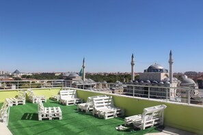 Terraza en la azotea con sillones blancos y una zona de césped artificial verde, con vistas a un paisaje urbano que incluye edificios históricos y alminaras.