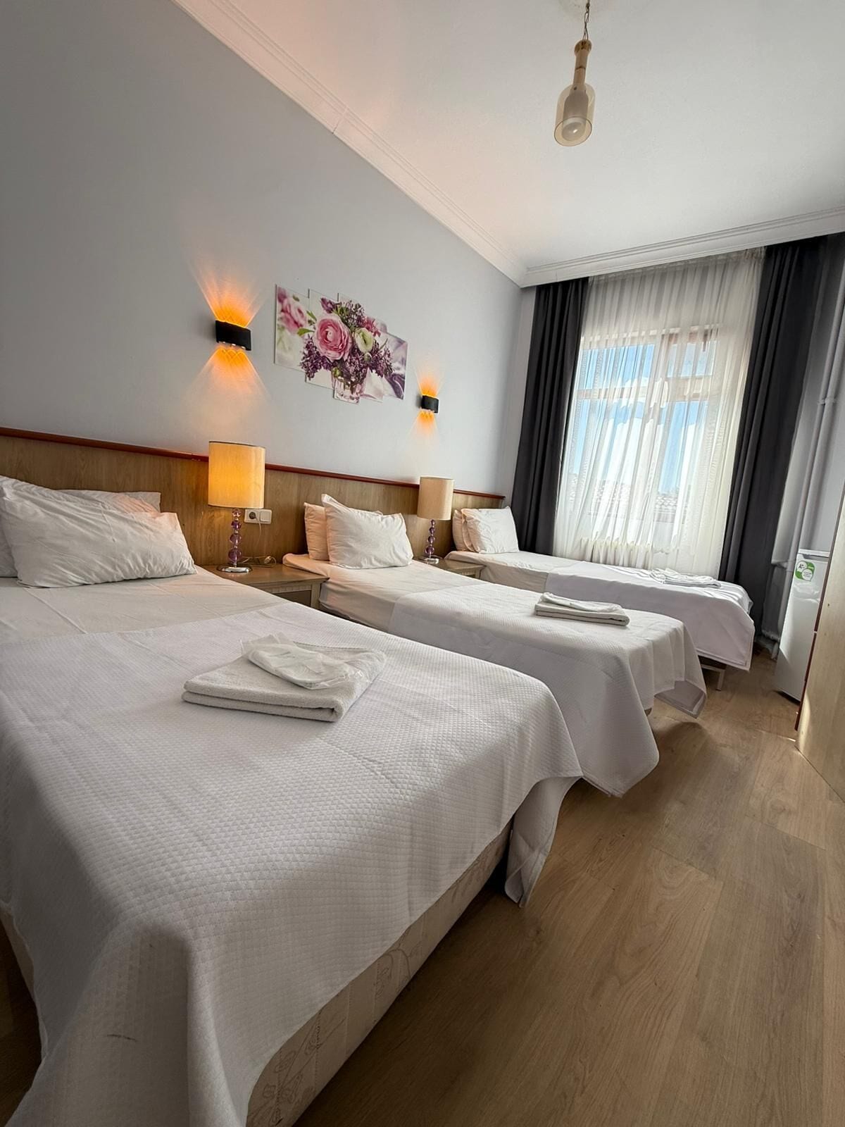 A hotel room with two beds, a wooden headboard, a floral artwork, and a window with curtains.