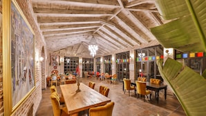 Uma sala de jantar espaçosa com mesas e cadeiras de madeira, paredes de tijolo e grandes janelas.