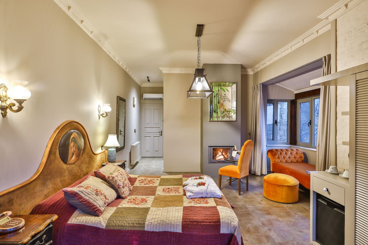A bedroom with a large bed, a chair, a small sofa, a fireplace, and a window.