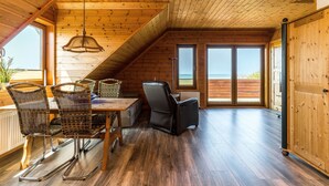 Interior de madera con zona de comedor, sillas, una mesa y vistas amplias a través de grandes ventanales.