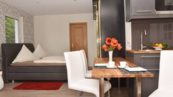 A modern living room with a sofa, a dining table with chairs, a red rug, and a kitchen area with a sink and cabinets.