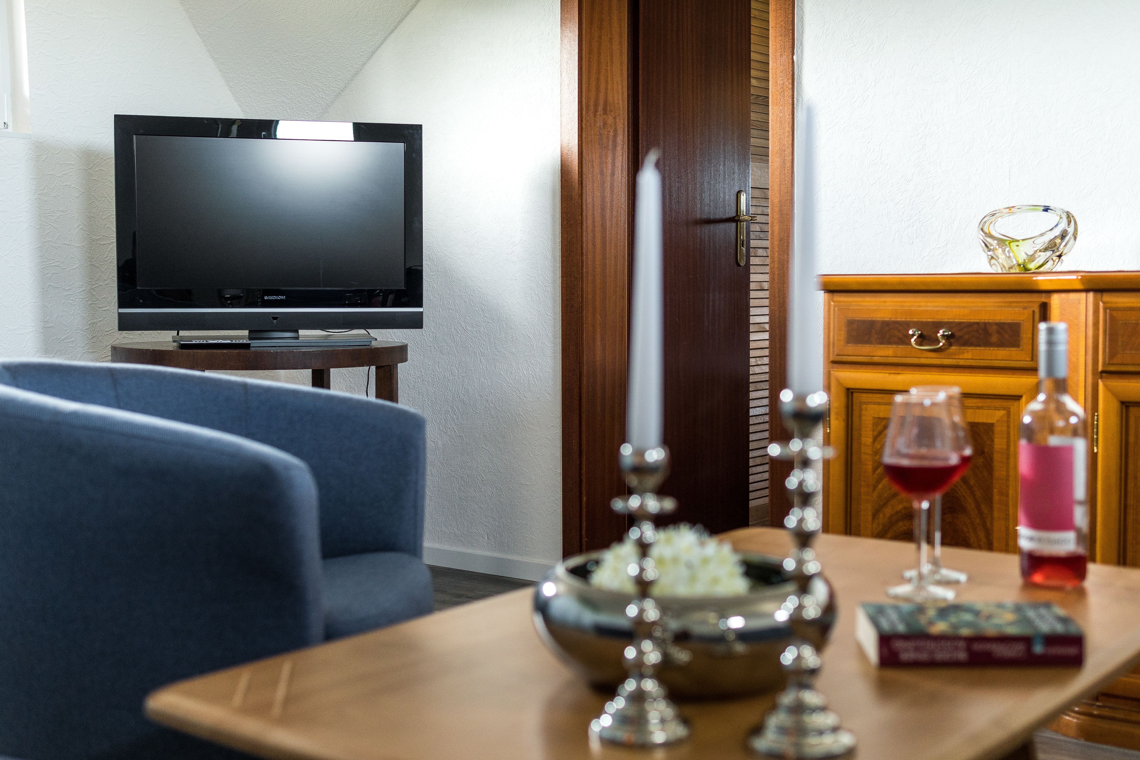 Een woonkamer met een televisie, een eettafel met een boek, een wijnglas en een kaars.