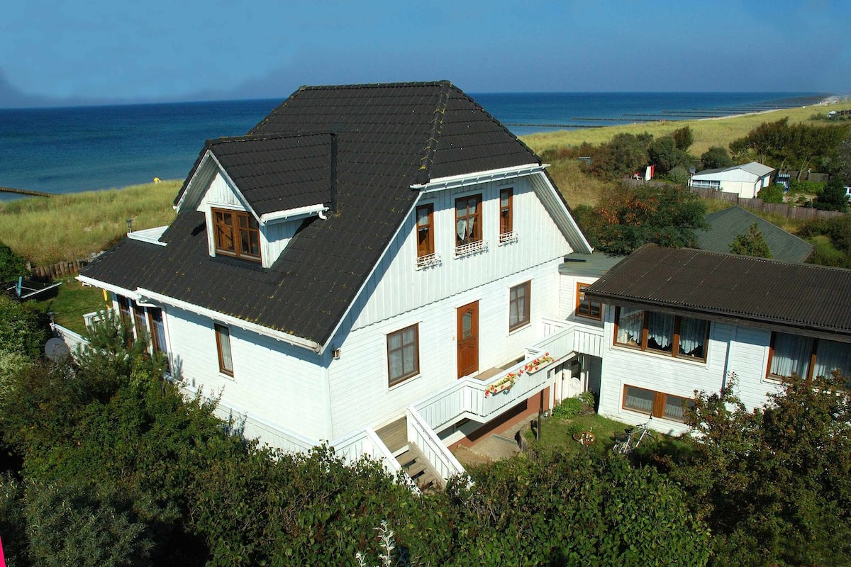 A two-story house with a dark roof, white exterior, and a balcony with railings.