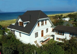 Una casa de dos pisos con techo oscuro, fachada blanca y un balcón con barandillas.