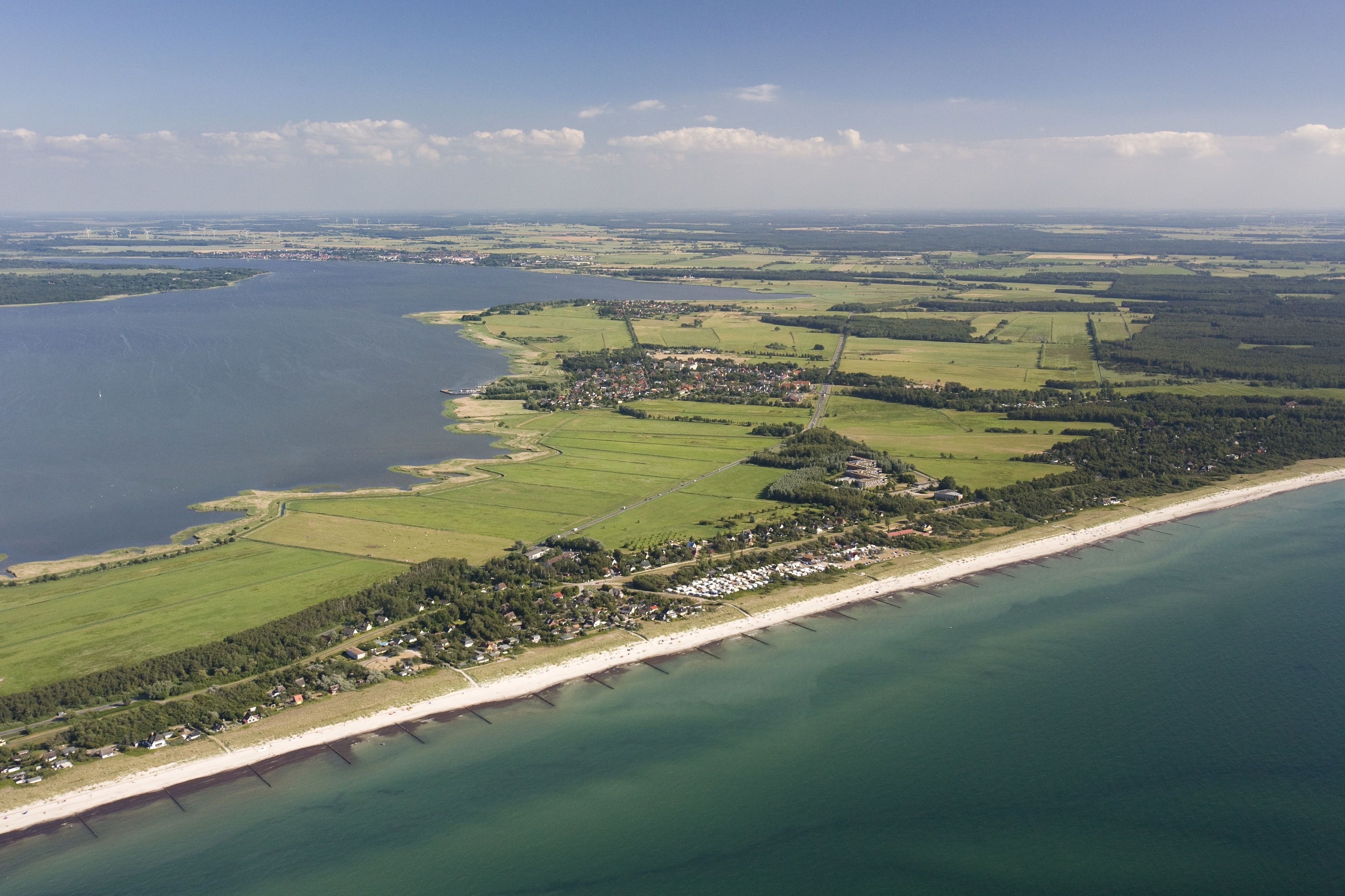 An aerial view of a coastal area with a beach, green fields, and a small town.
