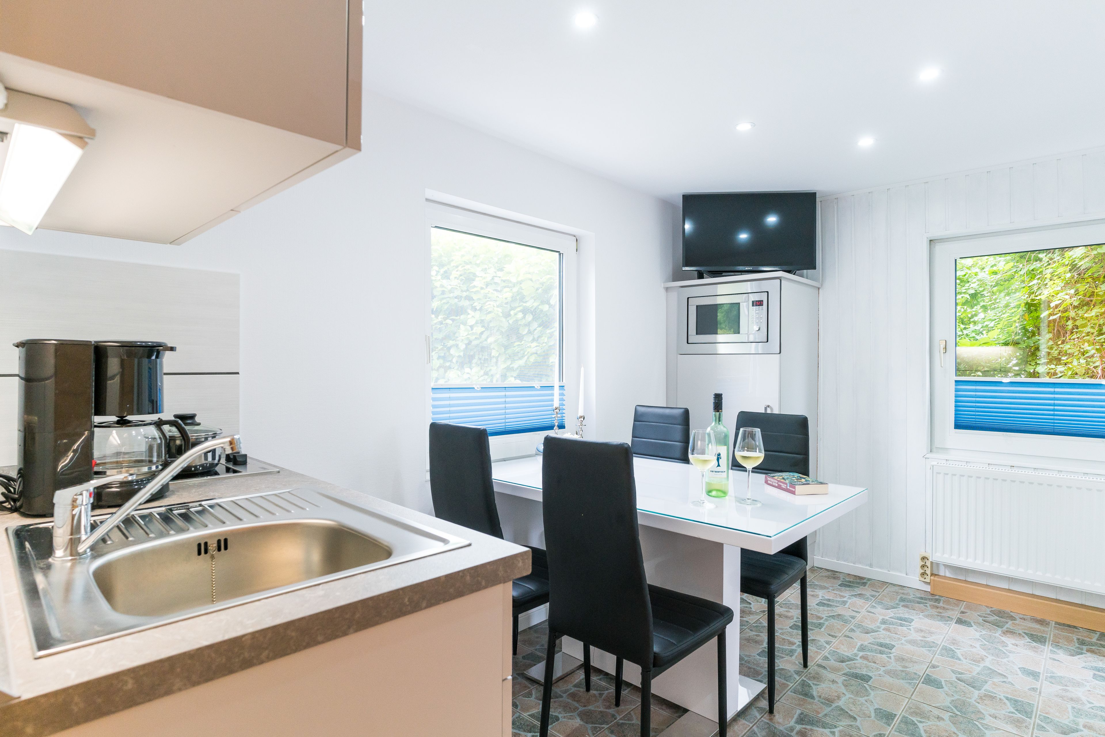 Cocina compacta con lavamanos, estufa y microondas. Hay una mesa de comedor con sillas y un televisor montado arriba.