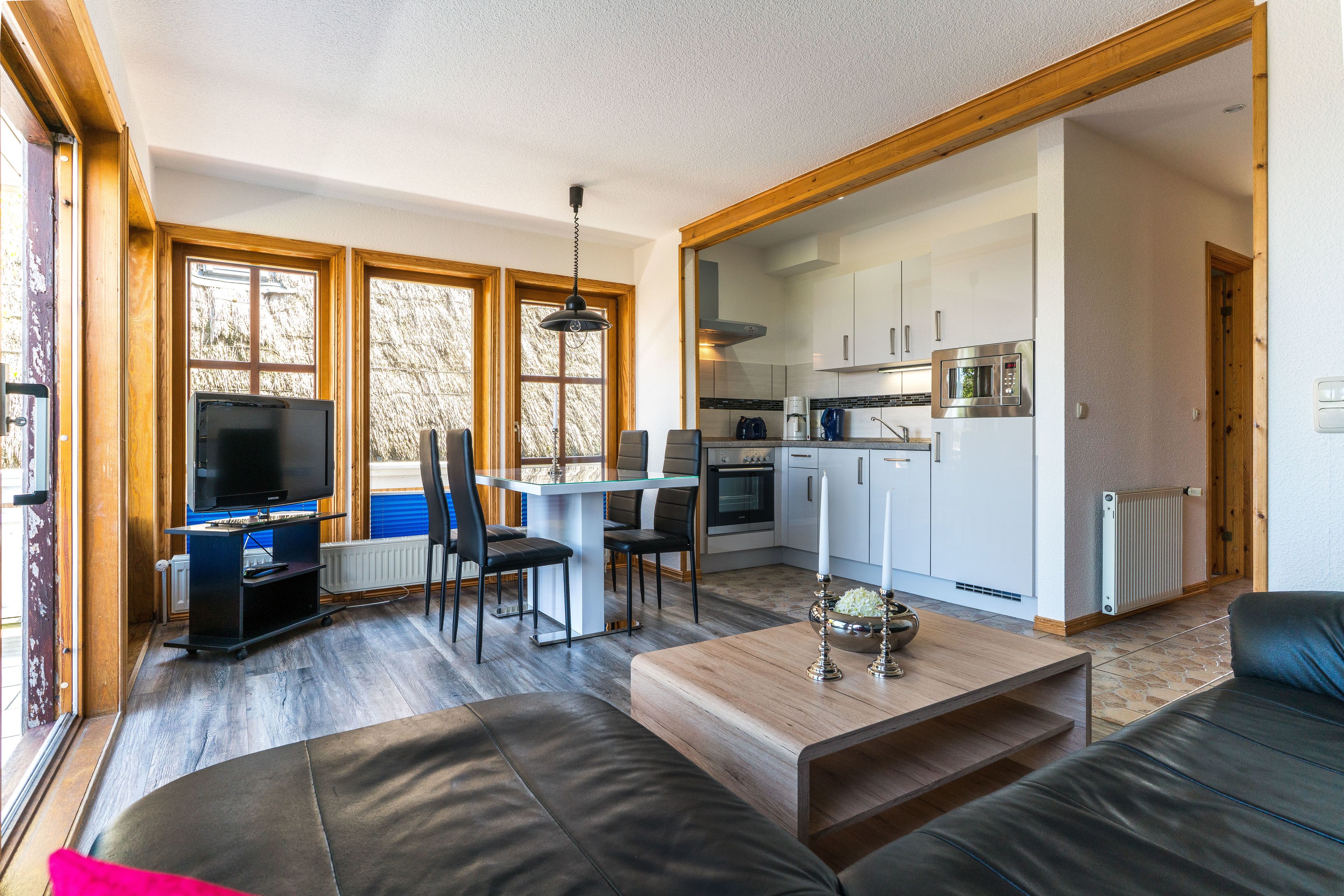 A modern living room with a large TV, comfortable seating, and a kitchen area with appliances.