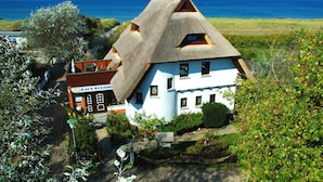 Una casa tradicional con techo de paja, fachada blanca, un jardín visible y vistas al mar.