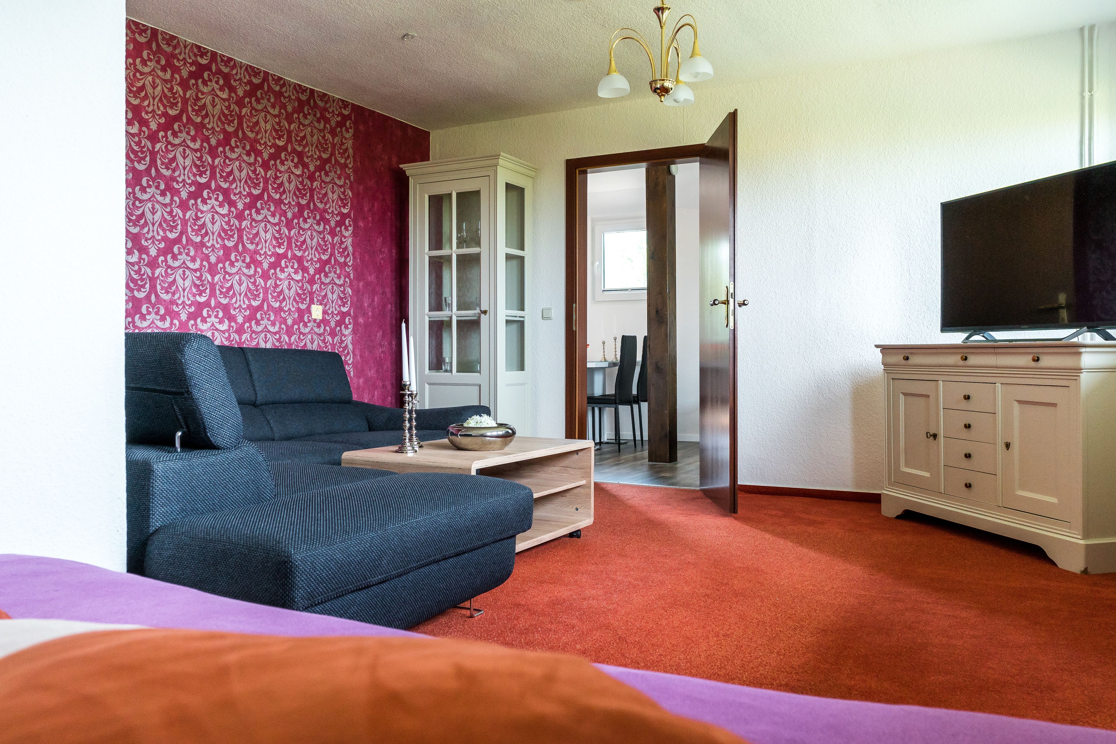 A room with a blue sofa, a wooden cabinet with a TV, and a patterned wall.
