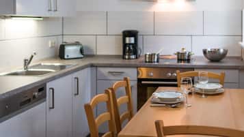 A modern kitchen with white cabinets, a wooden dining table, and a coffee maker.