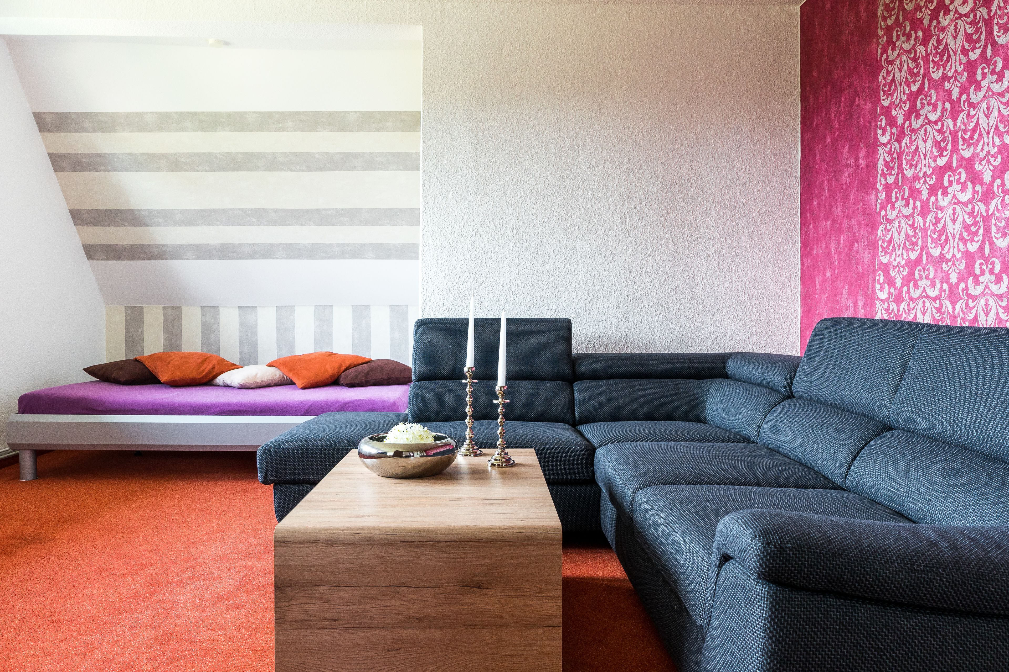 Una sala moderna con un sofá seccional, una mesita de madera y una cama con ropa de cama a rayas.