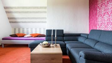 Una sala moderna con un sofá seccional, una mesita de madera y una cama con ropa de cama a rayas.