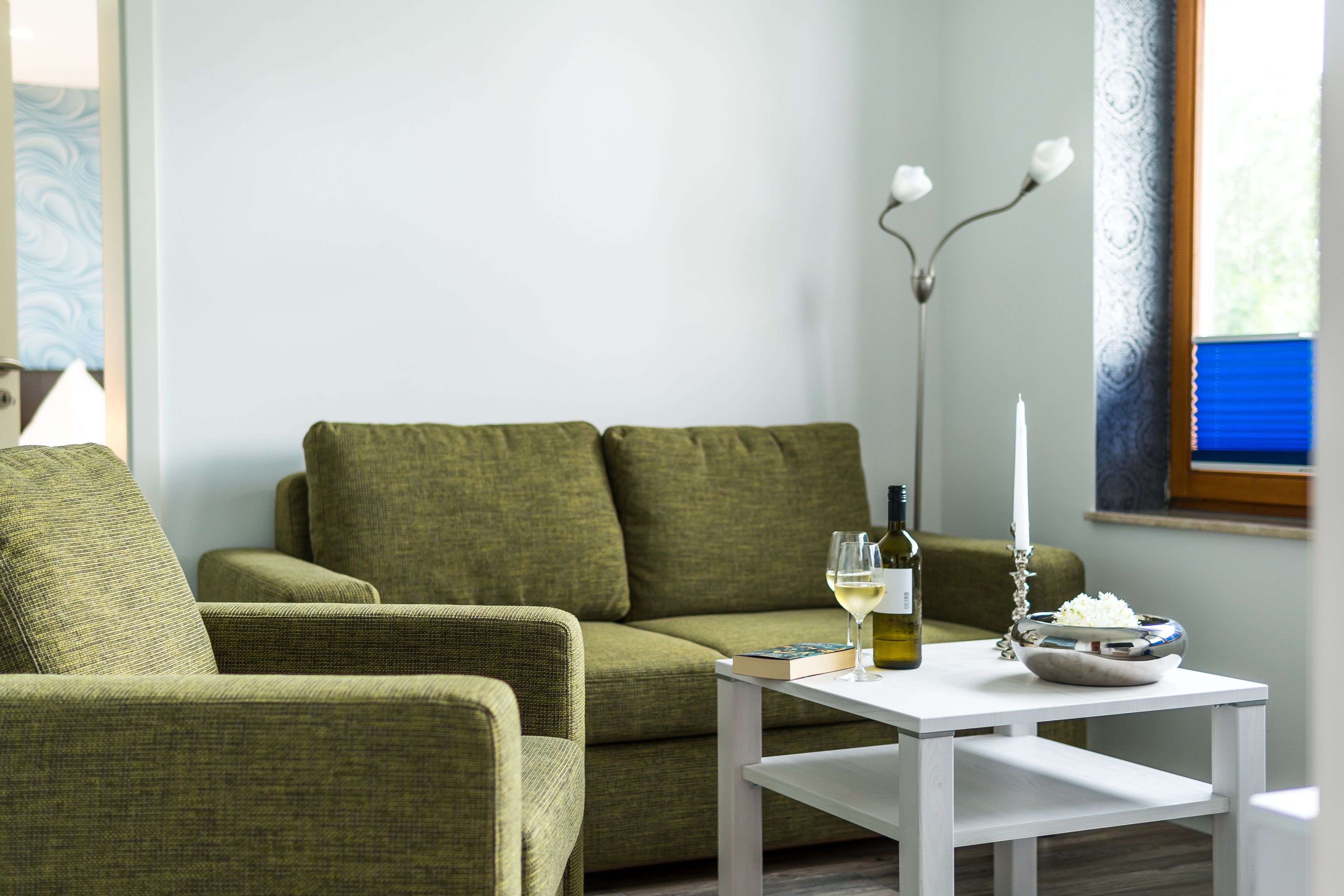 A living room with a green sofa, a white coffee table, a wine bottle, and a candle.