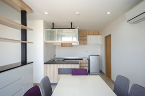 A compact kitchen with a white countertop, a built-in oven, and a refrigerator. There is a dining table with four chairs.